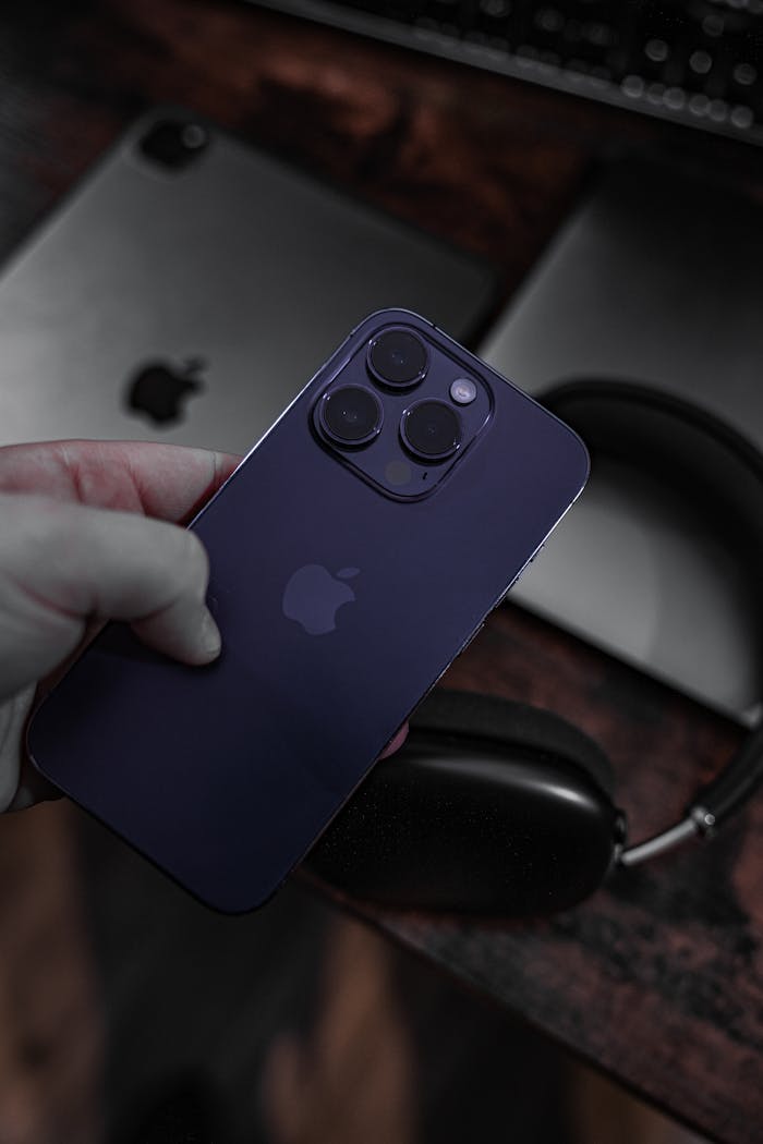 Close-up of a hand holding a smartphone with tech gadgets on a desk.