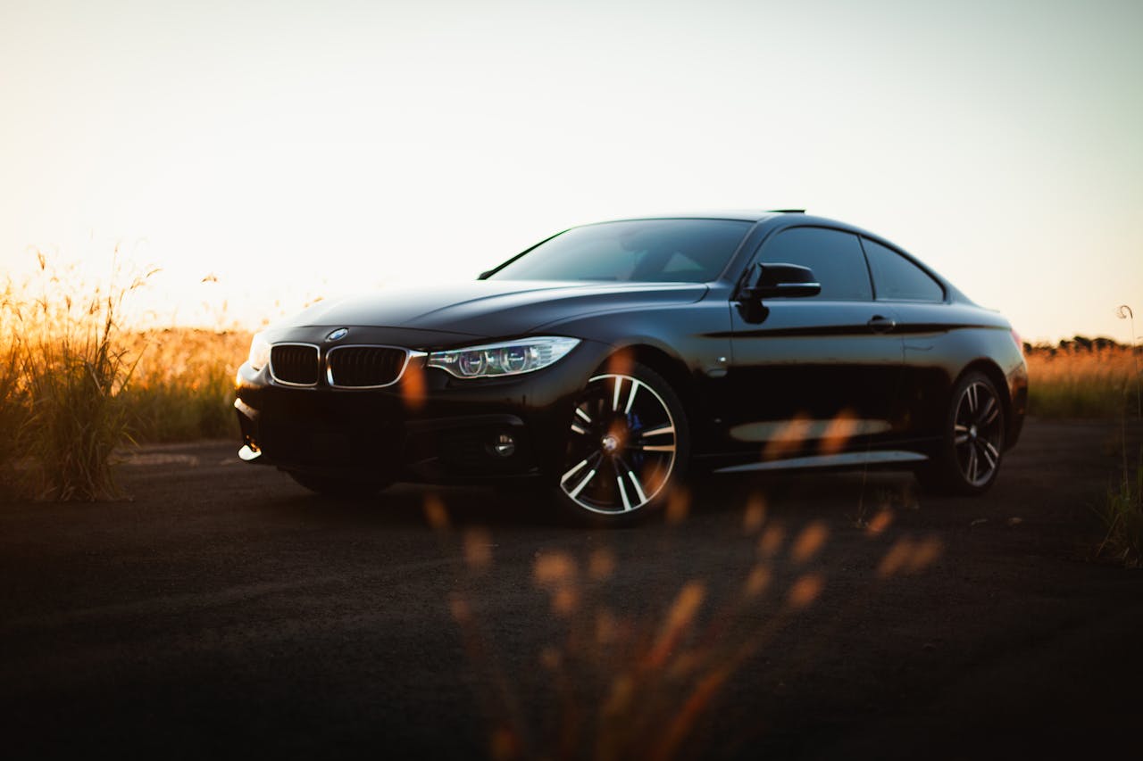 A black BMW 4 Series sports car parked on a rural road during sunset, capturing a serene and elegant moment.