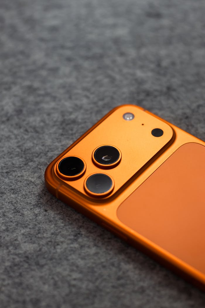 Stylish orange smartphone with triple camera lens on a gray fabric background, perfect for tech themes.