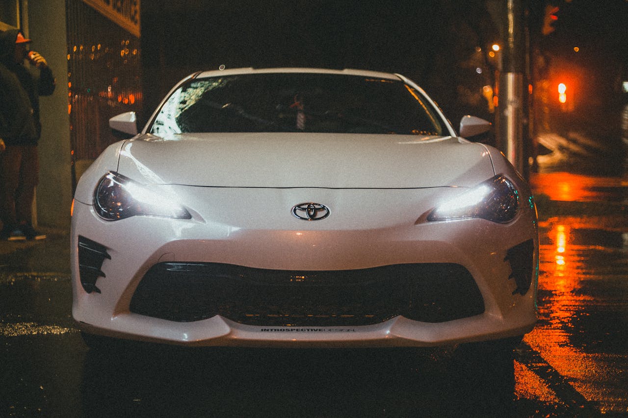 A white Toyota parked on a wet street at night, illuminated by city lights.